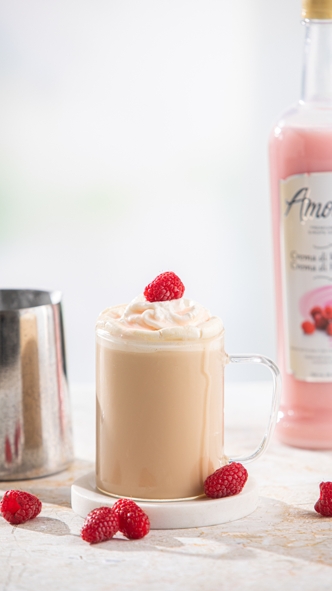 Raspberries and Cream Latte on a counter in front of Amoretti Crema di Raspberry Syrup surrounded by fresh raspberries