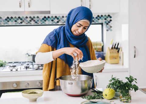 Aseel Tayah wears a blue hajib and sprinkles ingredients into a bowl in her kitchen for Lunch Lady Magazine