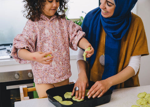 Aseel Tayah cooks with her daughter who stands on a chair to reach the bench