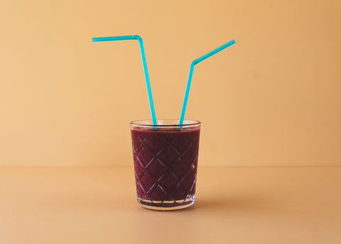 Photo of a persimmon, blackberry and lemon smoothie in a glass with two blue straw
