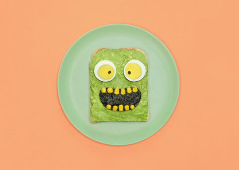 A photo of avocado on toast that looks scary with corn teeth and egg eyes