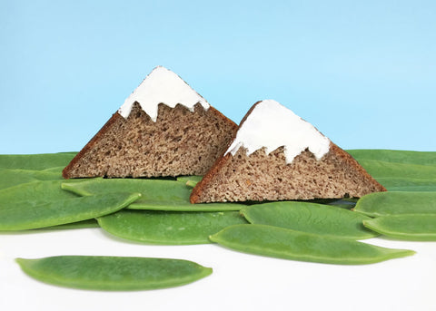 A photo of brown bread cut into triangles to look like mountains. Snow peas look like grass.