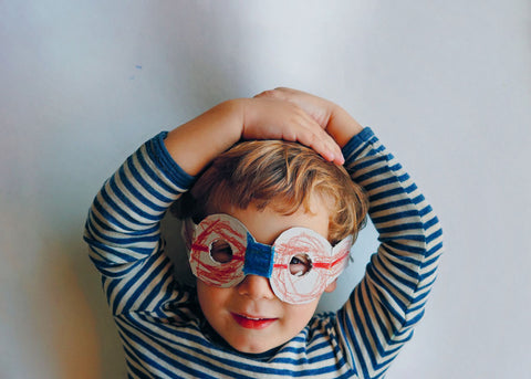 Photo of a small boy in a striped T-shirt wearing handmade paper glasses