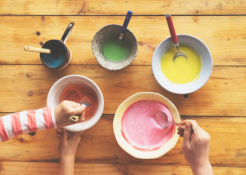 photo of five different bowls with coloured pikelet mixture and someone stirring them