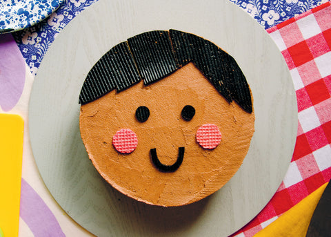 fun cake ideas: happy face cake - a brown face with black hair and rosy cheeks on a plate