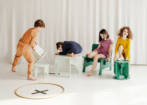 MiNiMONO furniture and four kids sitting on them against a white wall