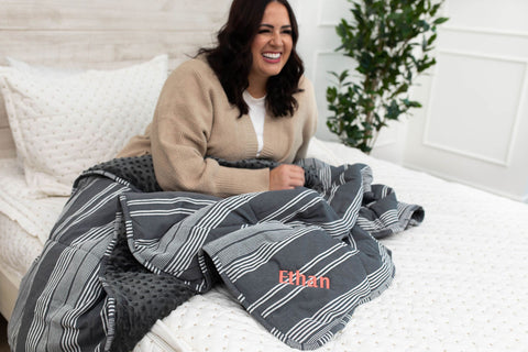 Woman sits on her Beddy's zipper bed with her embroidered personalized blanket.