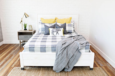 A guest room bed made with gray and white zipper bedding and yellow bedding accessories