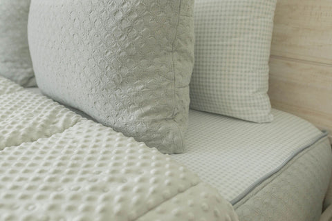 Close-up of white comforter and pillows on bed with green zippered bedding.