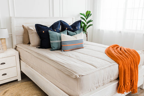 An image of Beddy's "Davis" on a white bed, with blue pillows and an orange throw.