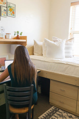 A woman sitting at a desk in a dorm room, with zipper bedding for dorm.