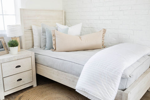 Minimalist white bed with headboard and nightstand, adorned with grey and white zippered bedding.
