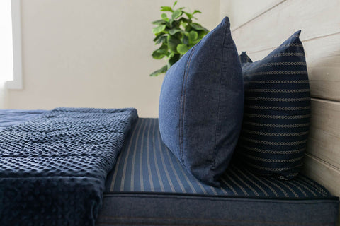 Denim zipper sheets adorn a bed with blue pillows and a plant.