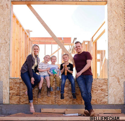 An image of a young family, woman, man and their three sons, stand in front of a framed home.