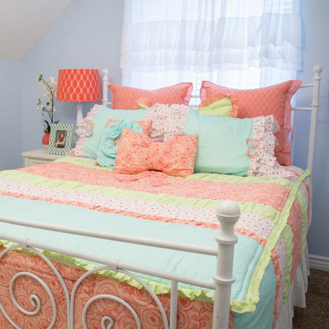 A girls room with a full size bed, made with green, blue, and pink zipper bedding