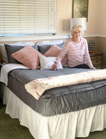 Image of an elderly woman sitting on the edge of her bed that features our Modern Gray Beddy's.