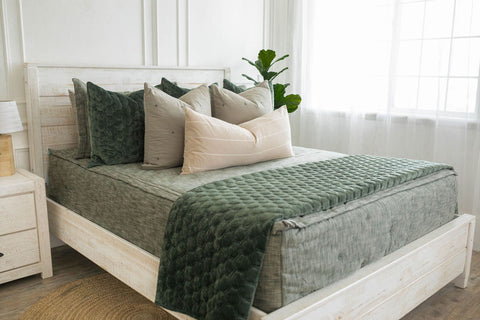 Bed with green and white pillows and a white nightstand, adorned with soft green zipper bedding.