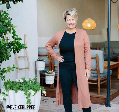 An image of a woman with short blonde hair standing in the doorway with her hand on her hip and some furniture seen behind her in the distance.