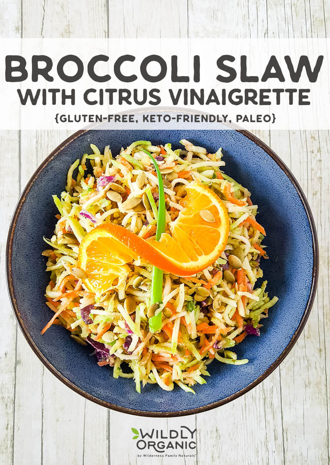 Top down photo of a blue bowl filled with broccoli slaw with a citrus vinaigrette with an orange and spring onion on top.