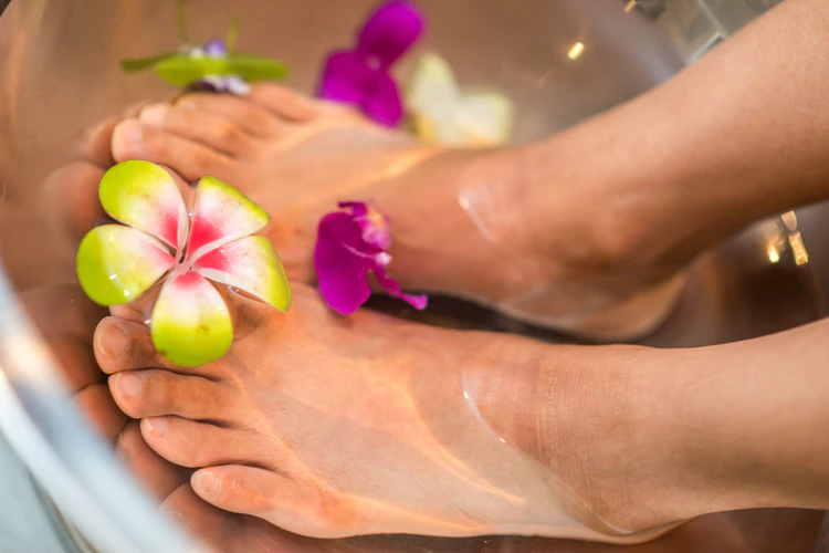 A person soaking their feet in a tub of water with floating flowers