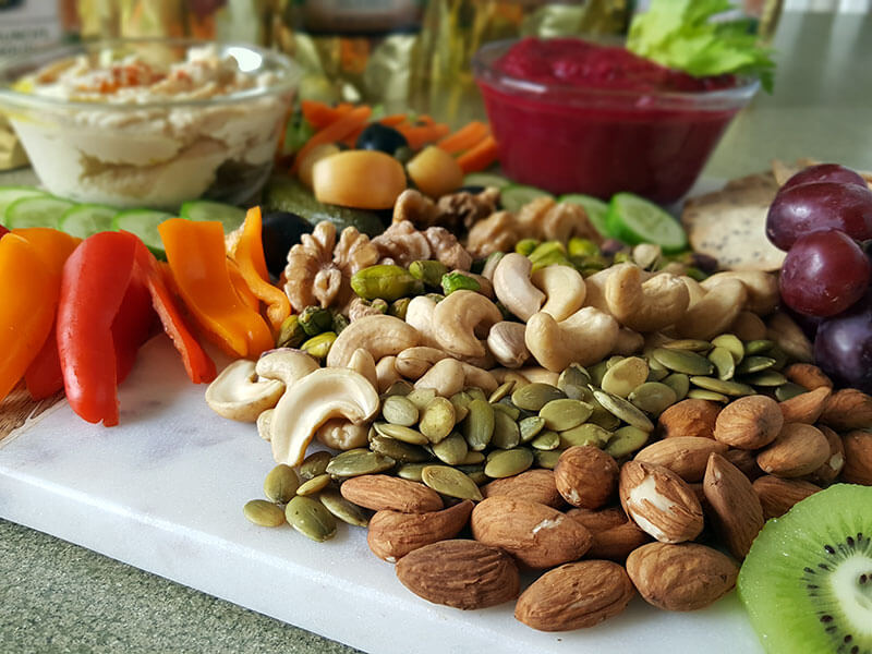 A photo of a selection of nuts and seeds, sliced veggies, dips, and other vegan foods. 