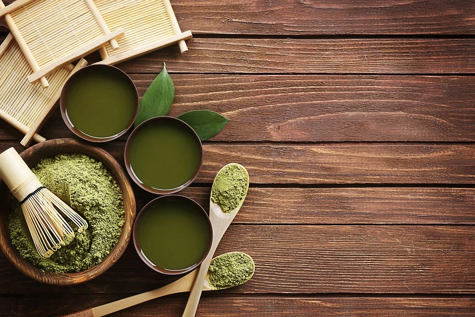 Green matcha powder and drinks inside bowls, cups, and spoons, on a wooden surface