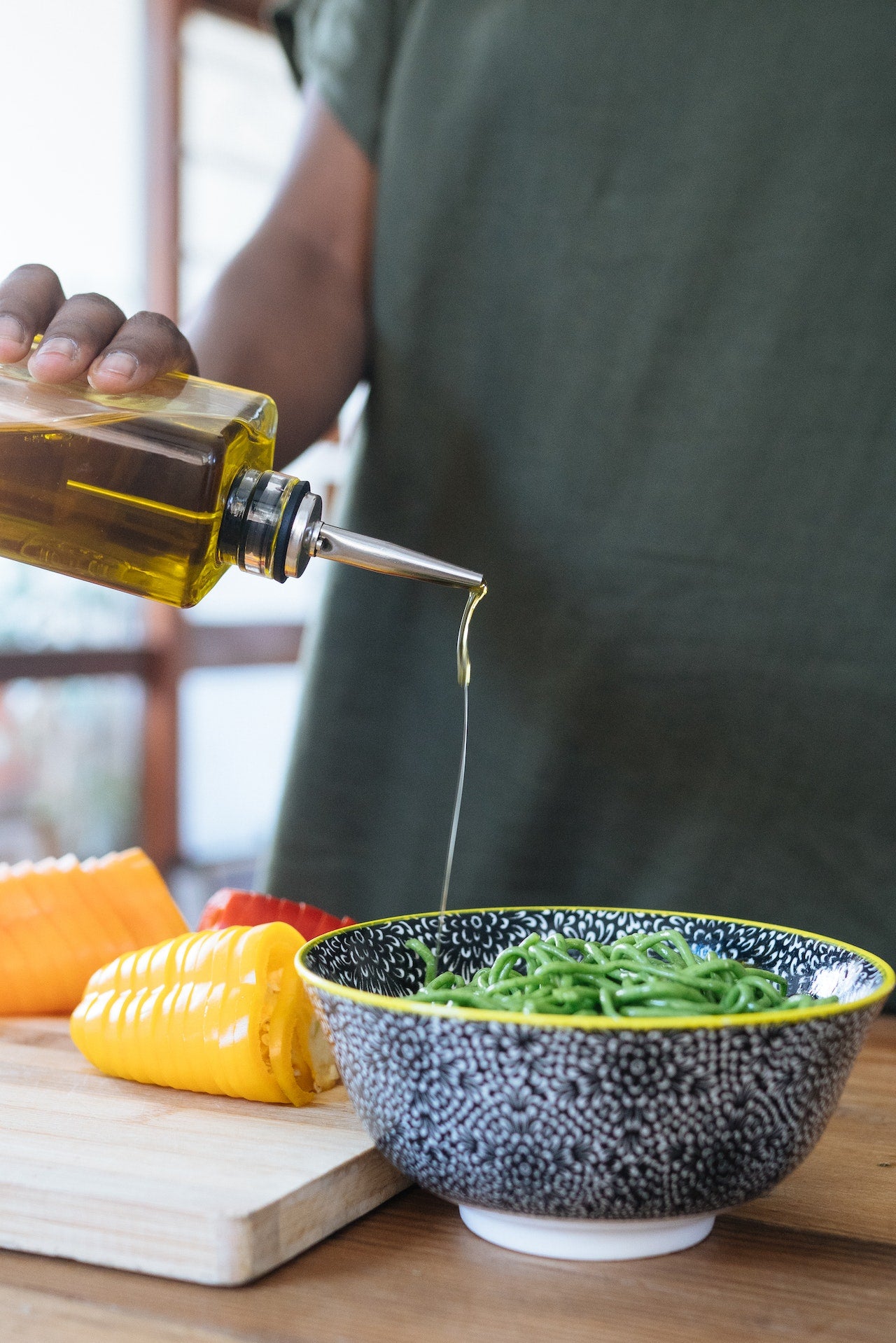 A man pouring olive oil over green noodles