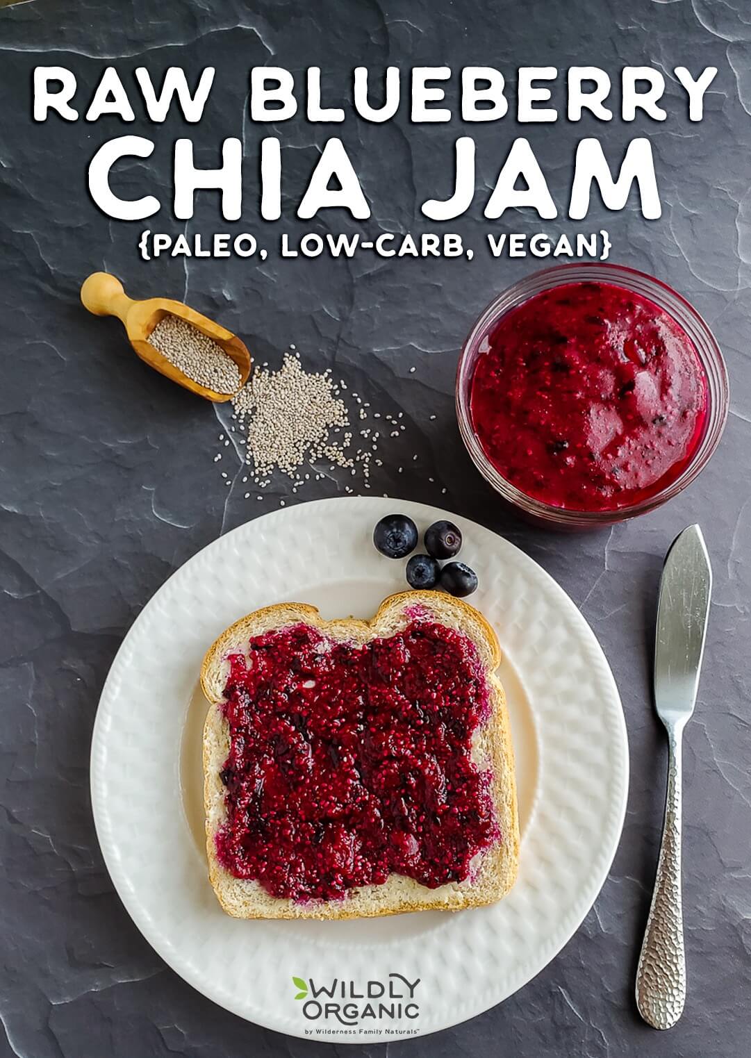 A photo of a piece of toast on a plate with raw blueberry chia jam on top with a bowl of chia jam on a table.