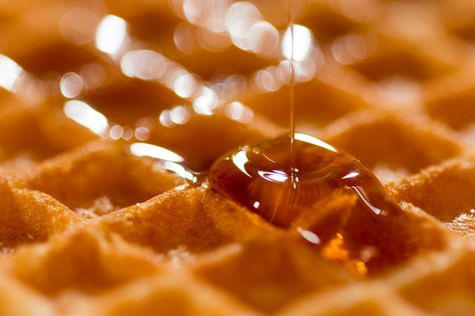Drizzling golden brown syrup on a waffle
