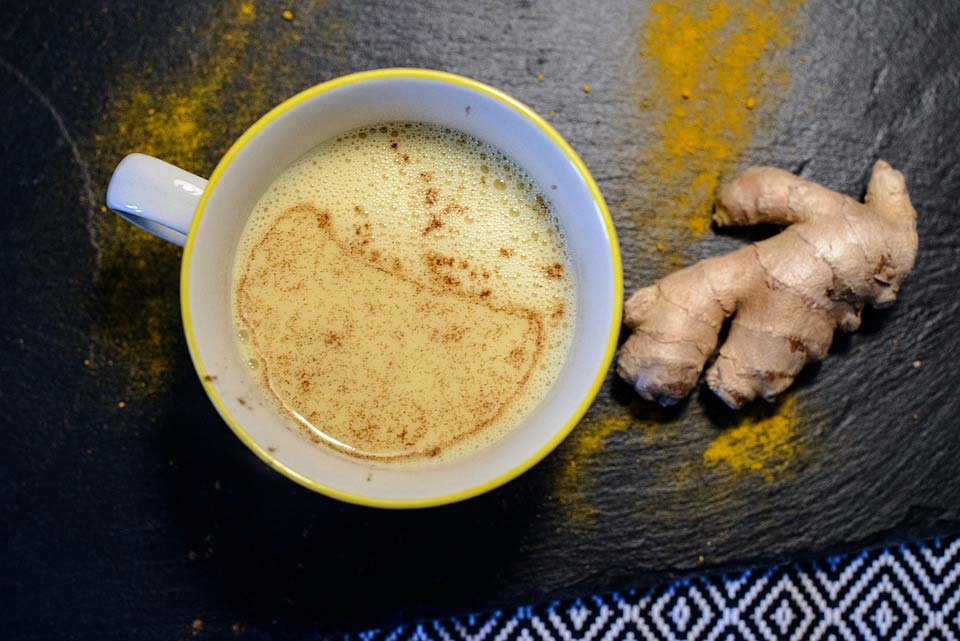 A ginger root placed next to a ceramic mug containing a creamy yellow beverage