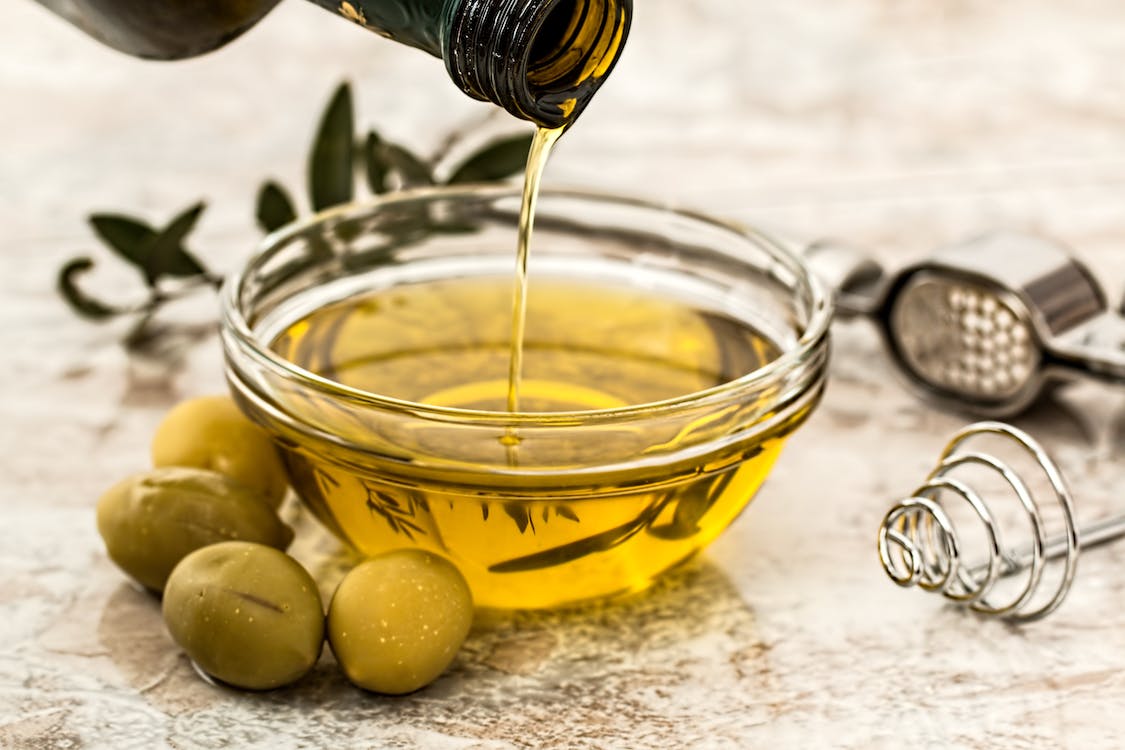 Pouring oil in a bowl next to olives