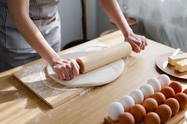 A woman rolling dough with eggs and butter on the side