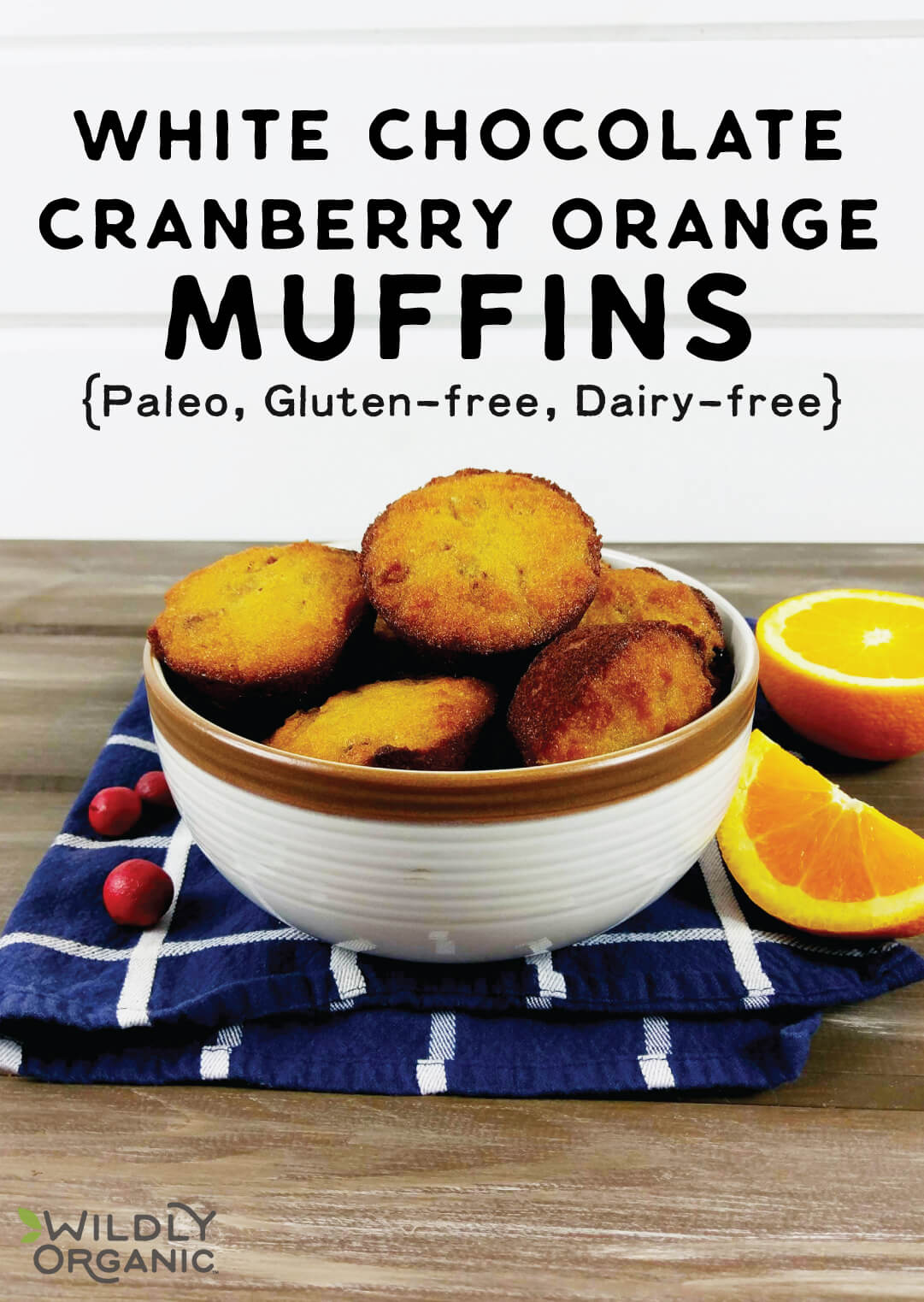 A bowl with paleo white chocolate cranberry orange muffins in them with fresh cranberries and orange slices.