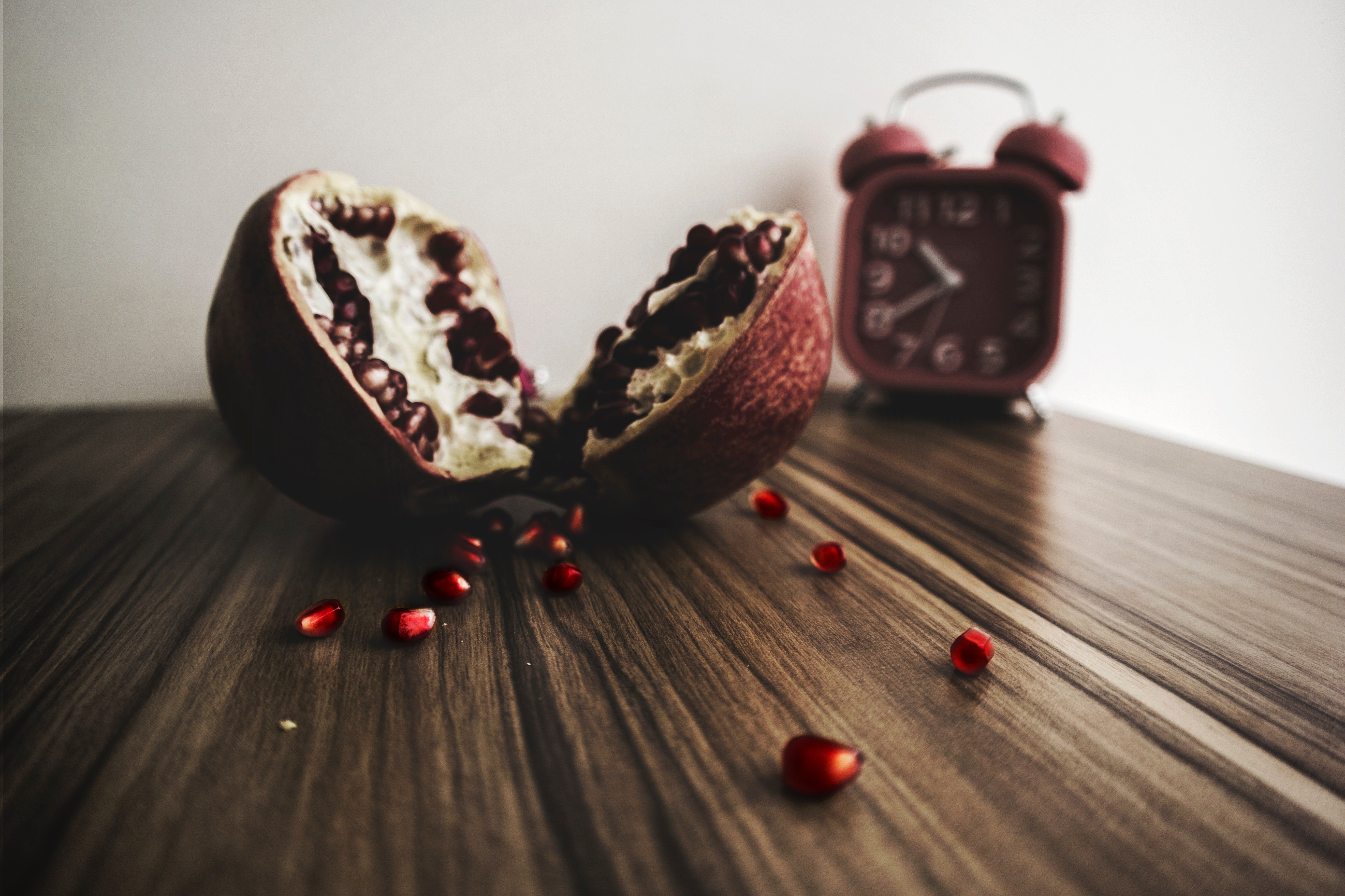 Pomegranate on a wooden table with a red clock