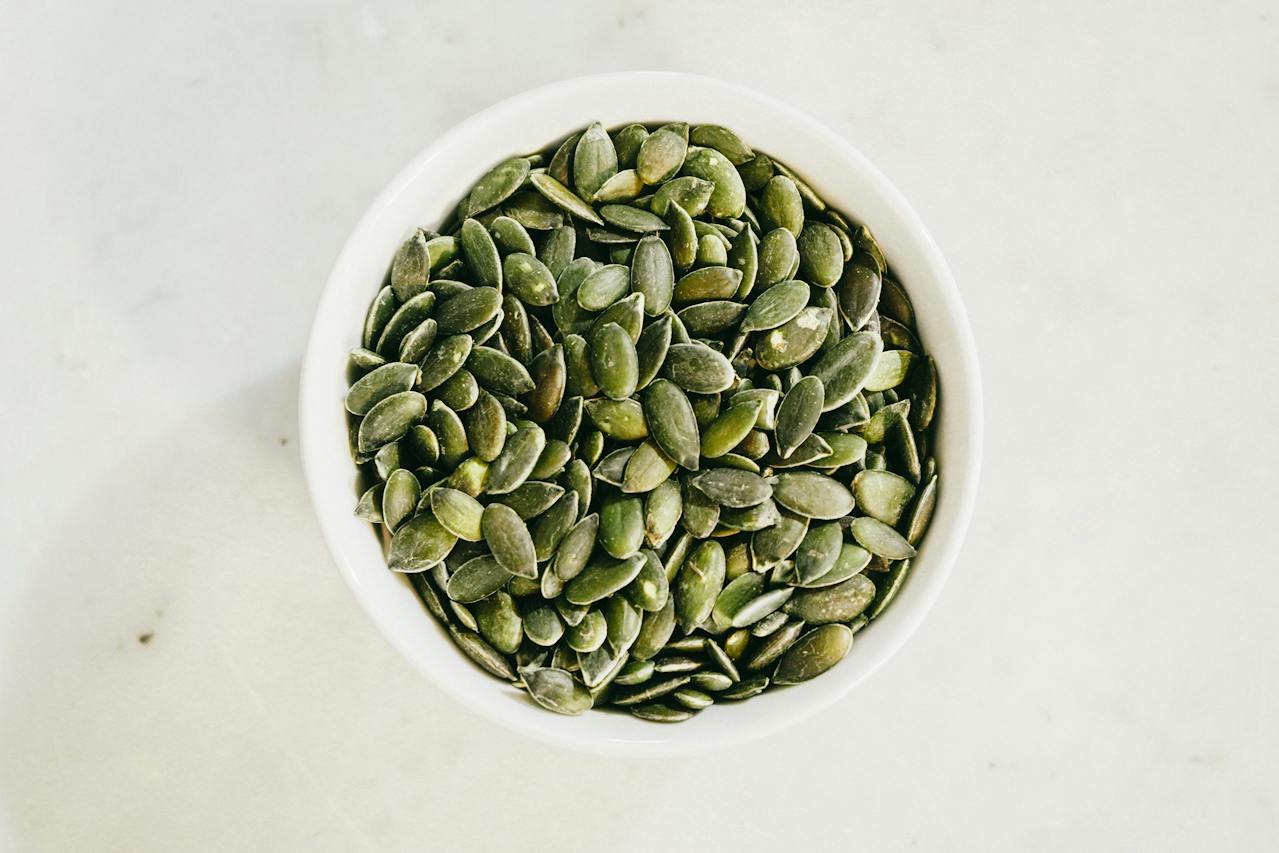 Overhead photo of pumpkin seeds in a white bowl on a white countertop