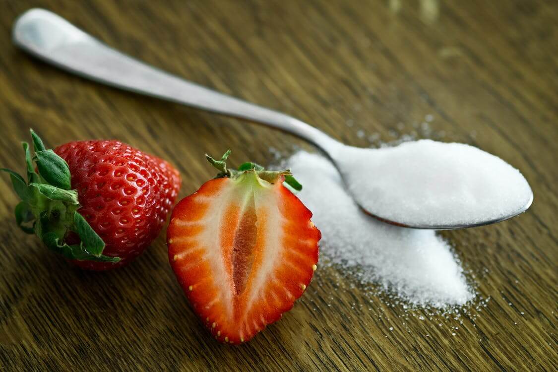 strawberries beside a spoon of refined sugar