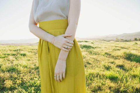 Jennie Kwon model wearing rings and bracelets on both hands in sunny field