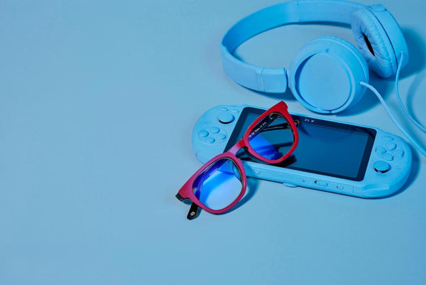 Blue light gaming glasses, a pair of headphones, and a portable gaming console
