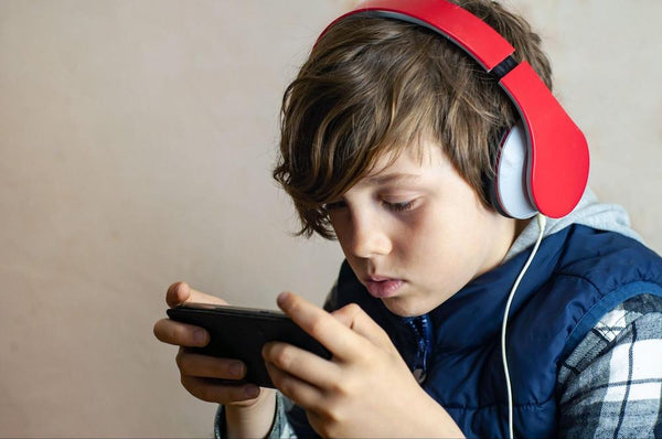 A boy wearing red headphones and staring closely at a video game device.