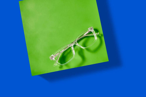 A pair of clear eyeglasses sitting on a green block on top of a blue background.