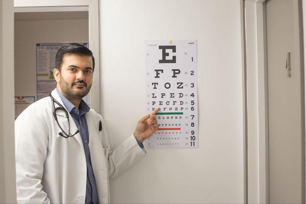 20/40 vision: A male eye doctor pointing to a vision test chart with rows of letters on it.