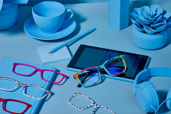 Eyeglass frames, headphones, tablet, and a cup on a blue table