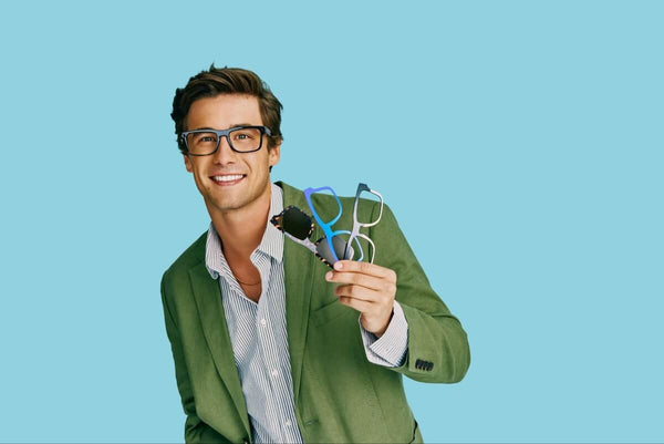 Man holding 3 pairs of eyeglasses while wearing a pair of eyeglasses