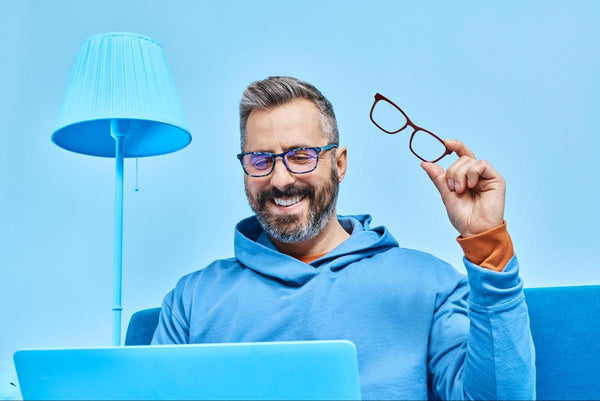 Man holding a pair of eyeglasses while using a laptop