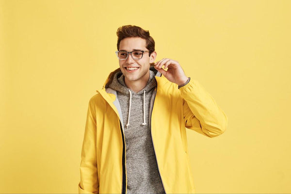 A man wearing a yellow jacket and glasses in front of a yellow background.