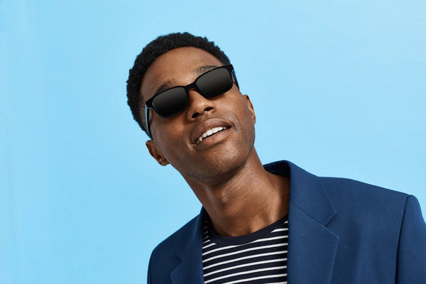 A man in front of a blue background wearing black sunglasses.