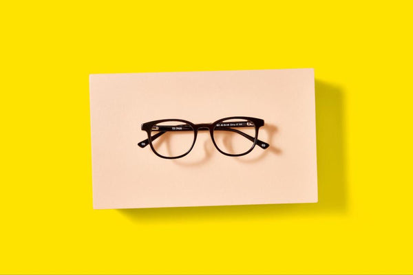 A pair of dark round eyeglasses on a yellow background from Pair Eyewear.