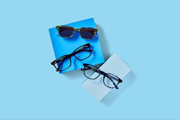Bifocal vs. progressive: Two pairs of glasses and a pair of sunglasses sitting on a blue background.