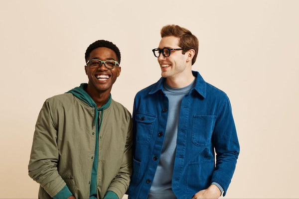 Two smiling men wearing glasses in front of beige background.