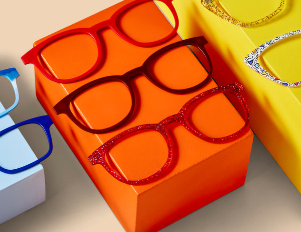 A variety of red and orange glasses for heart-shaped faces sitting on an orange block.